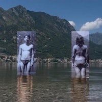 a photo of two people standing in the water with mountains in the background